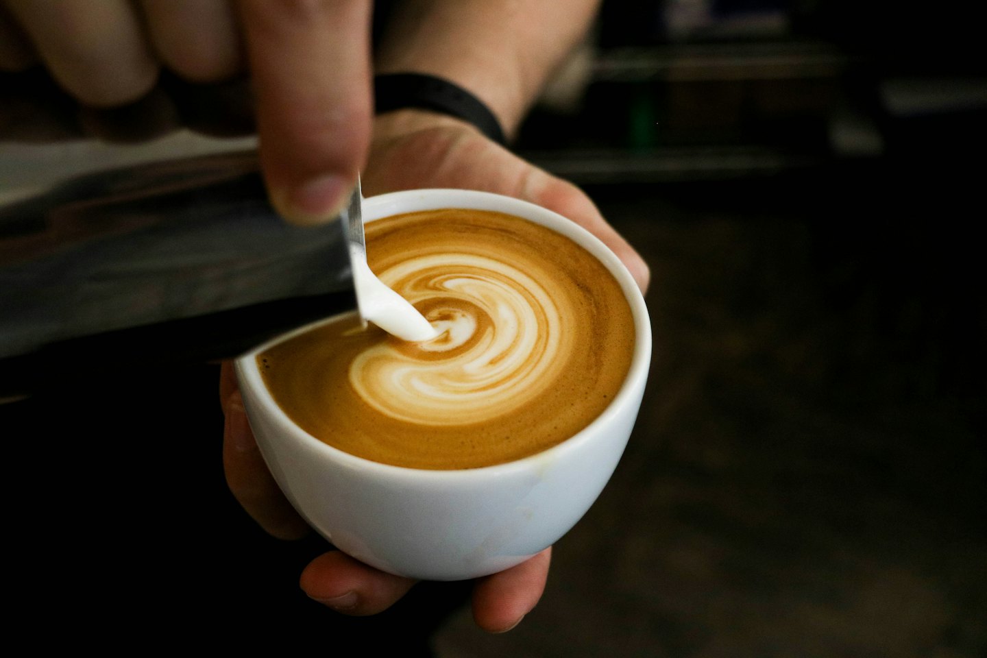 Barista pours frothed milk into a cup to create latte art.
