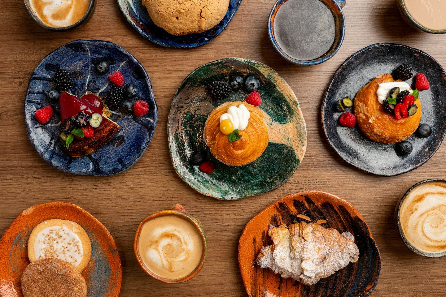 Assorted pastries and coffee mugs arranged on a wooden table.
