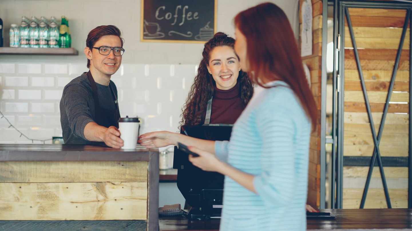 Barista smiling and handing a coffee cup to a customer.