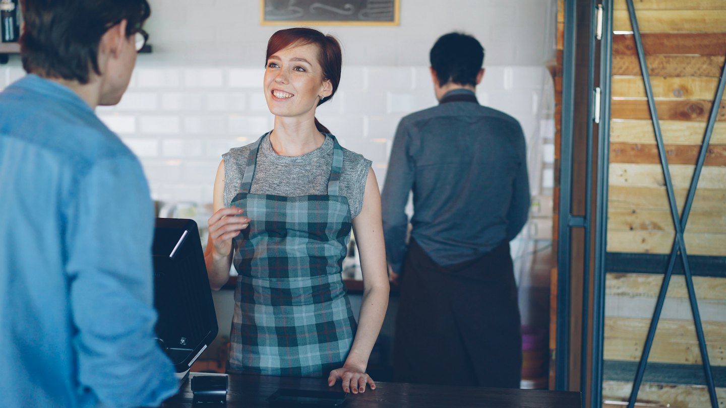Barista smiles while serving a customer at the cafe counter.