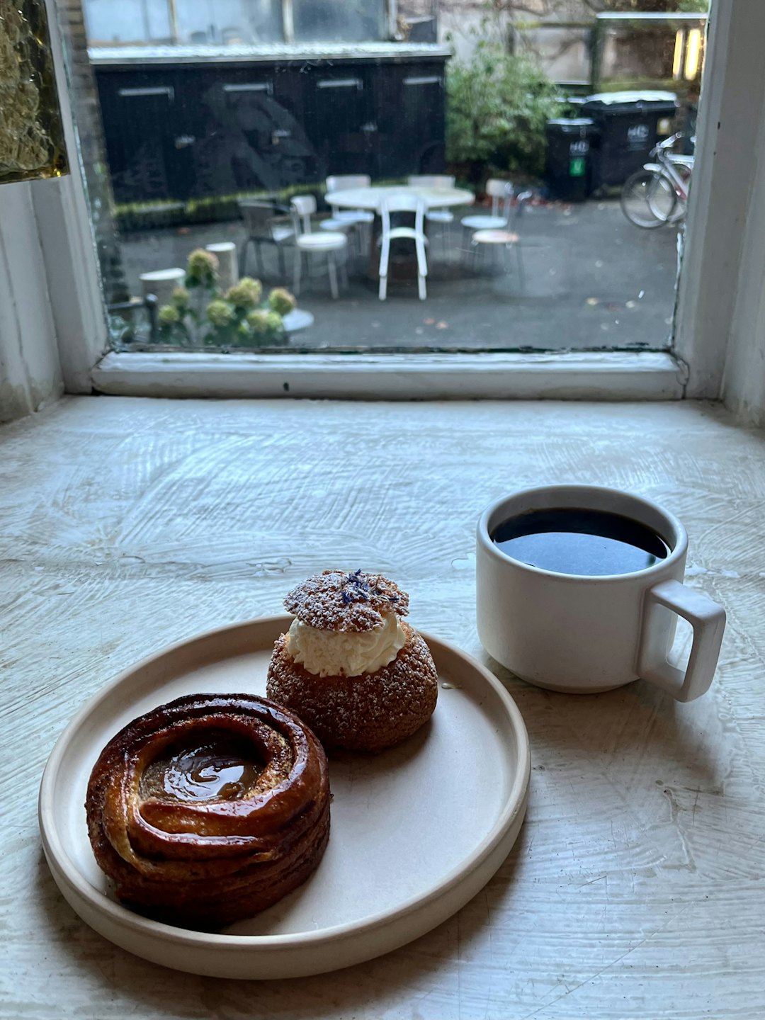 Two gourmet pastries and black coffee sit on a plate.