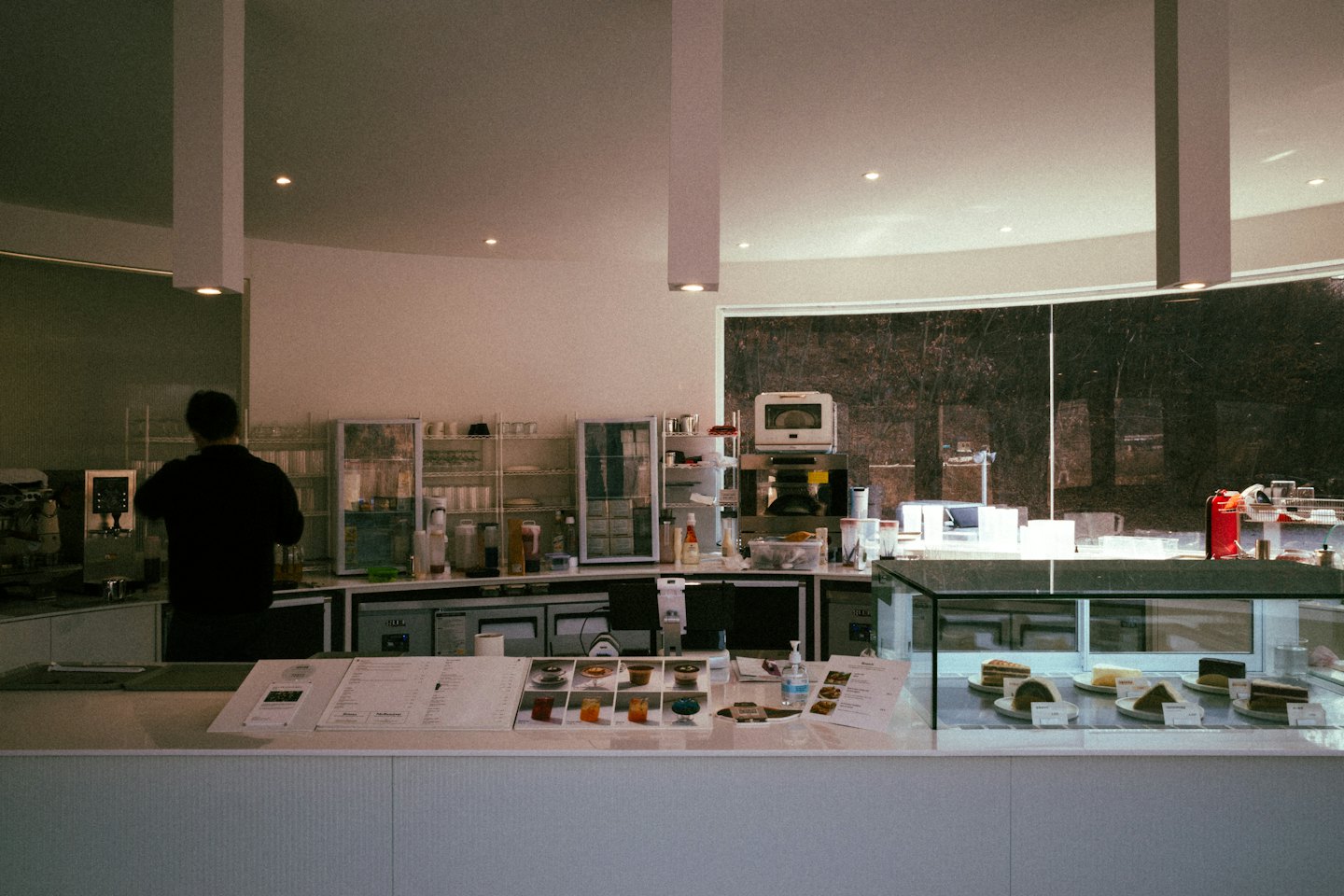 A barista works behind a modern cafe counter with pastries.