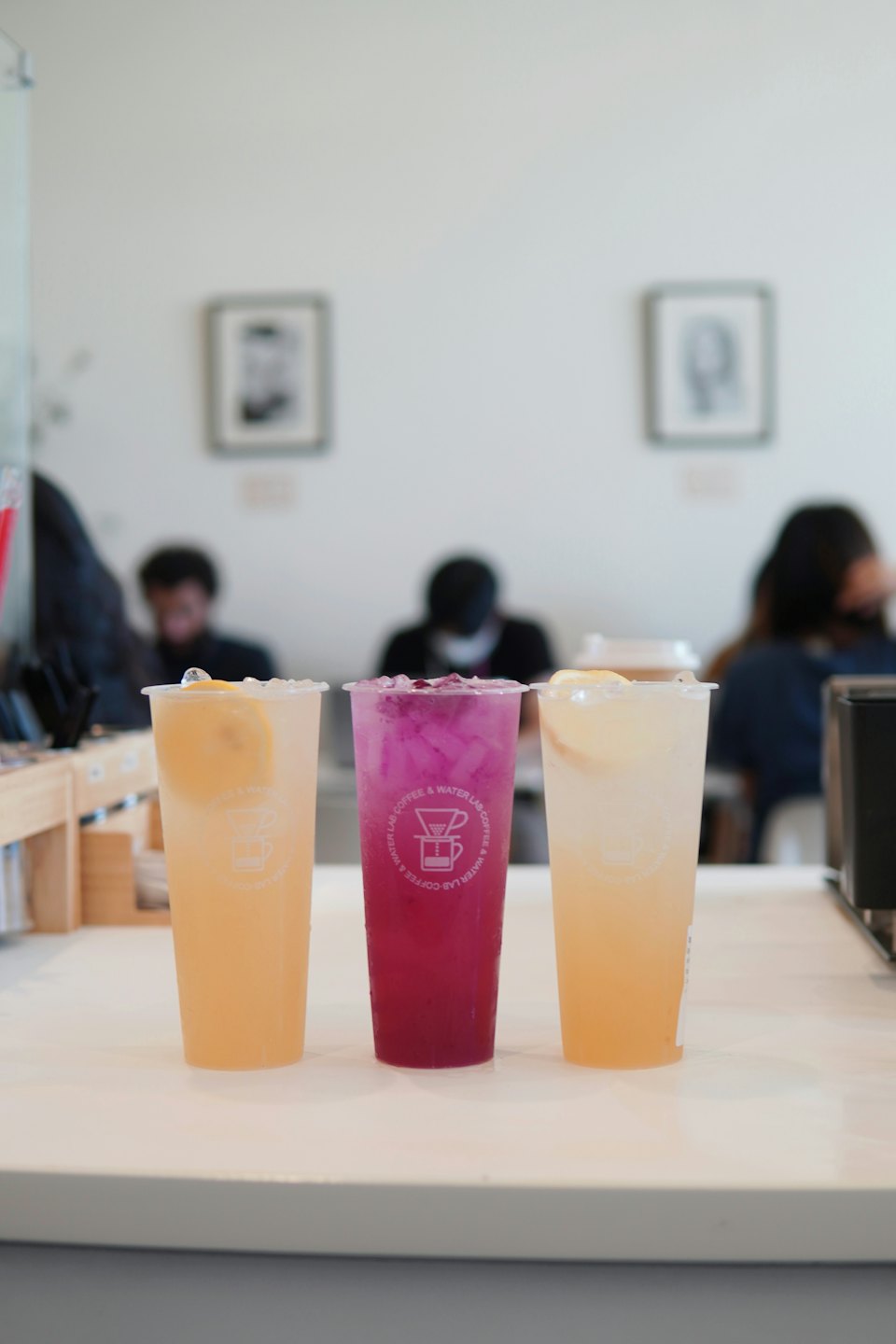 Three iced drinks in plastic cups sit on a counter.